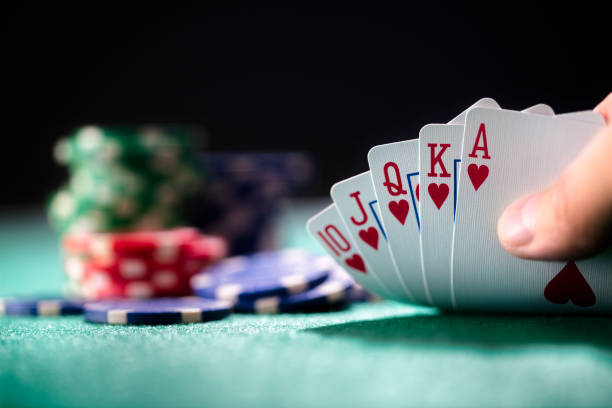 Close-up of a royal flush in hearts held next to a stack of poker chips on green felt.